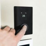 Hand pressing a button on a black smart thermostat