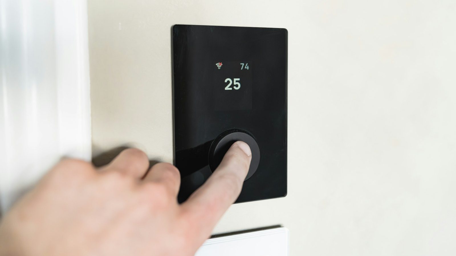 Hand pressing a button on a black smart thermostat