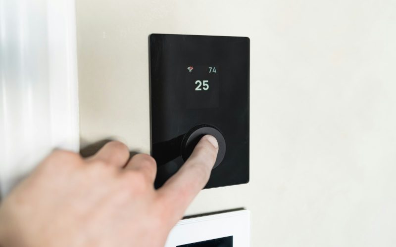 Hand pressing a button on a black smart thermostat