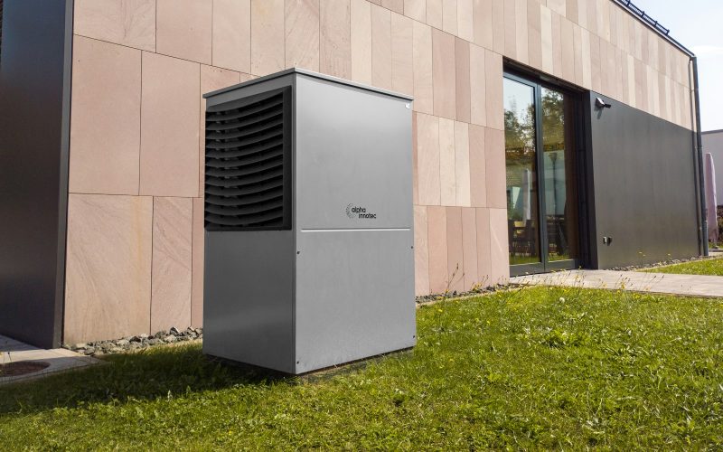 Modern outdoor heat pump unit next to a stone-clad building