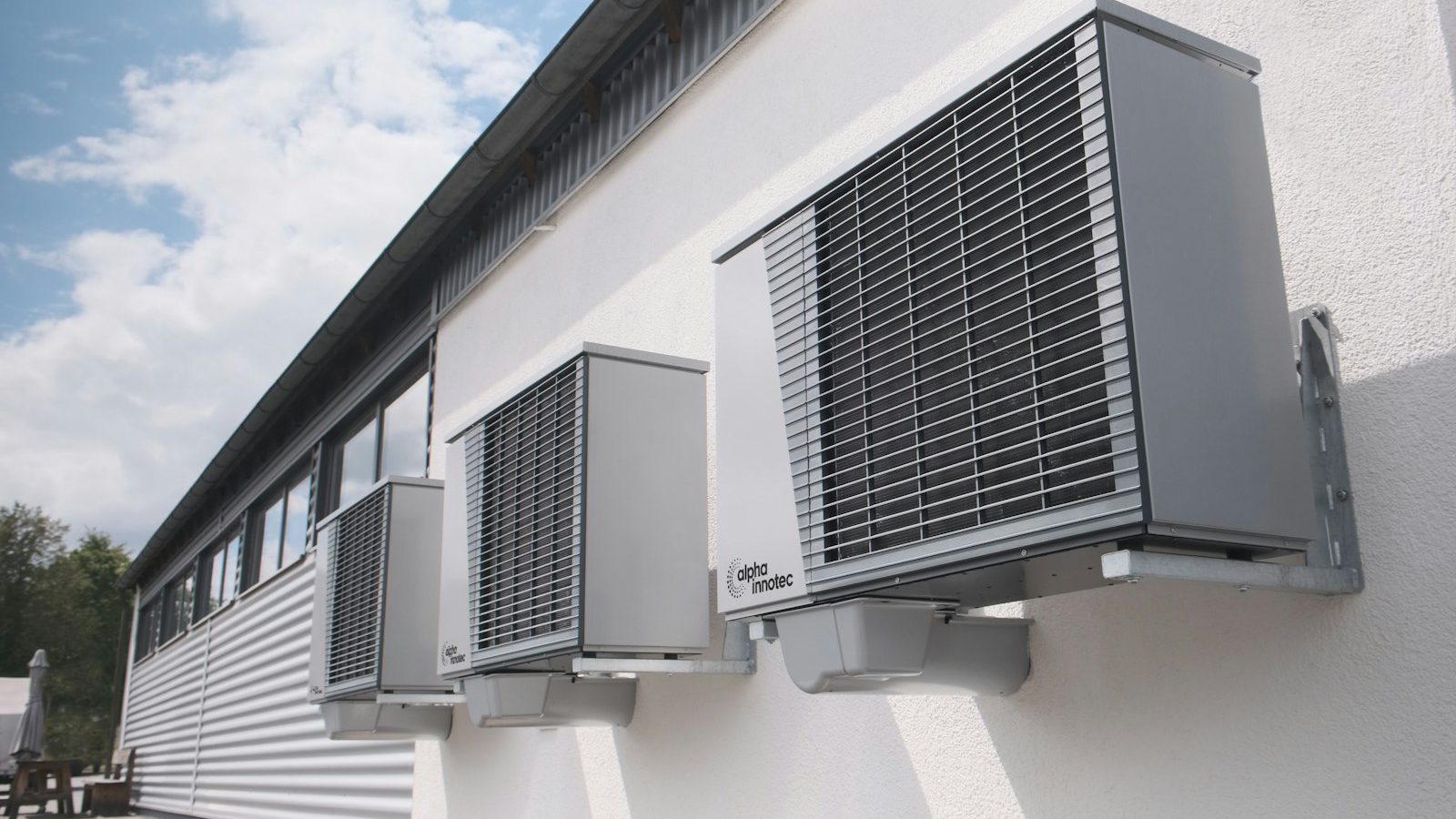 Three gray heat pump outdoor units mounted on a white wall
